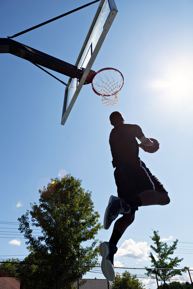 Back lit silhouette of a basketball player going up for a reverse jam.