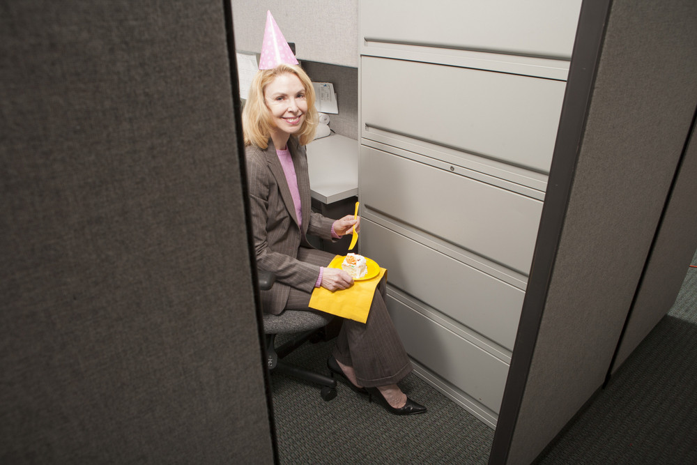 Business person eating birthday cake in cubicle