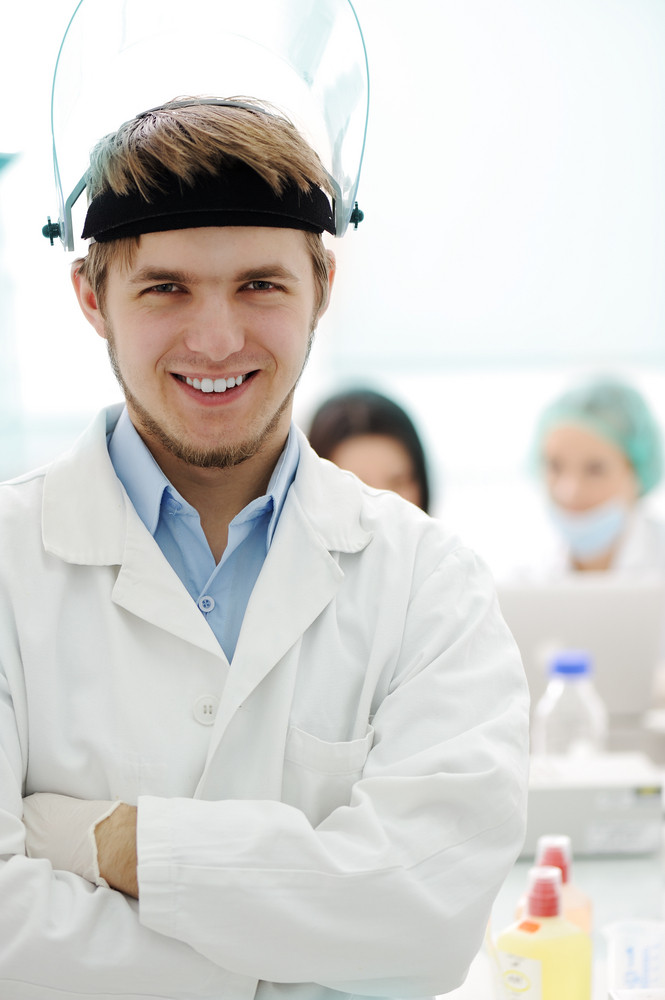 Confident young doctor with mask and folded hands in hospital laboratory