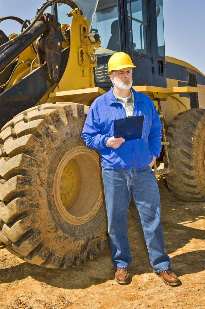 Construction Worker With Clipboard and Earthmoving Equipment