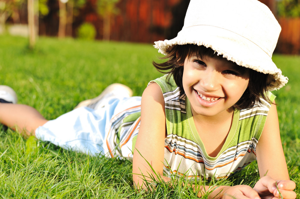 Cute kid with hat on head laying on grass in park