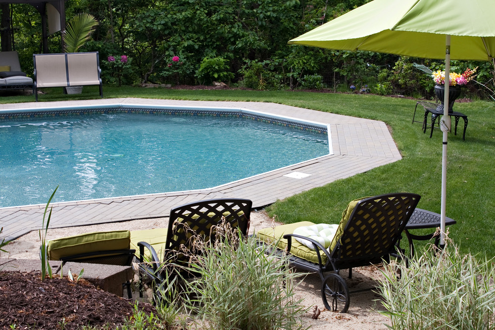 Detail view of a luxurious in ground pool and patio lounge. This partly wooded backyard garden offers the same level of luxury found in many vacation resorts.