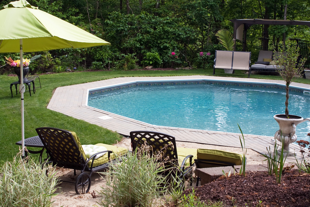 Detail view of a luxurious in ground pool and patio lounge. This partly wooded backyard garden offers the same level of luxury found in many vacation resorts.