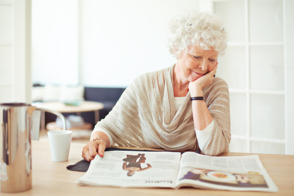 Elegant grandmother sitting at home reading a magazine