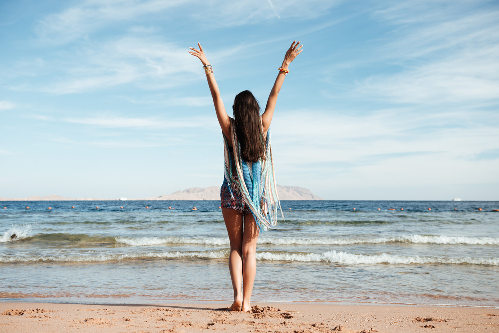 Back view of Woman in beachwear which standing on the beach with hands ...