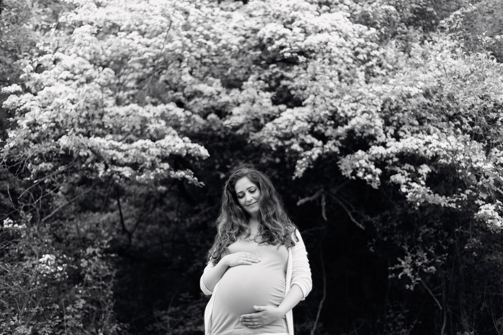 Beautiful pregnant woman wearing pink t-shirt holding her belly. Sunny summer nature. Black and white portrait.