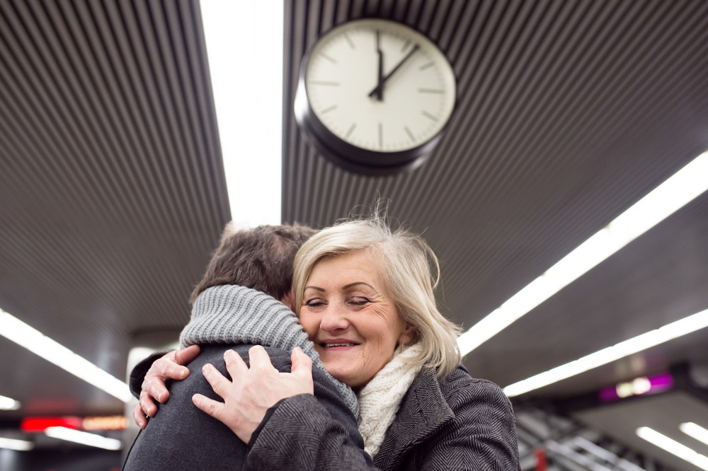 Beautiful senior couple standing at the underground platform, hugging. Welcoming or saying good bye. Five past twelve.