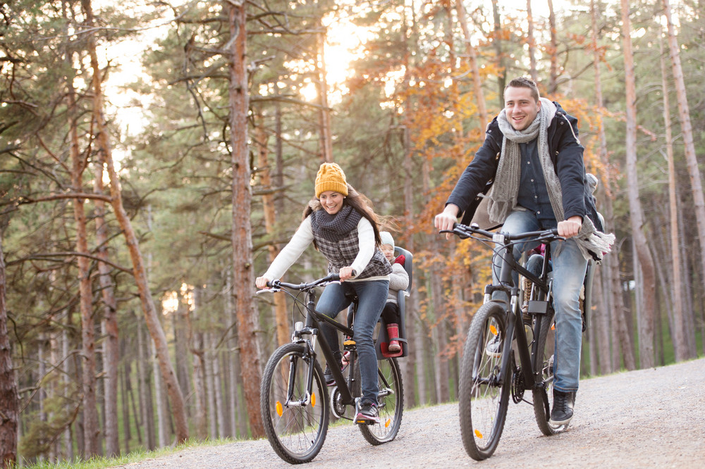 Beautiful young family with two daughters in bicycle seats in warm clothes cycling outside in autumn nature