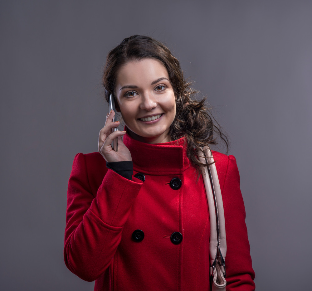Beautiful young woman in red coat with smart phone. Studio shot on ...