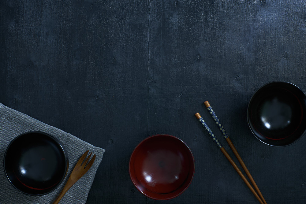Black color wooden table top view. On the table are the Japanese wooden spoon, chopsticks, bowl and table linen.