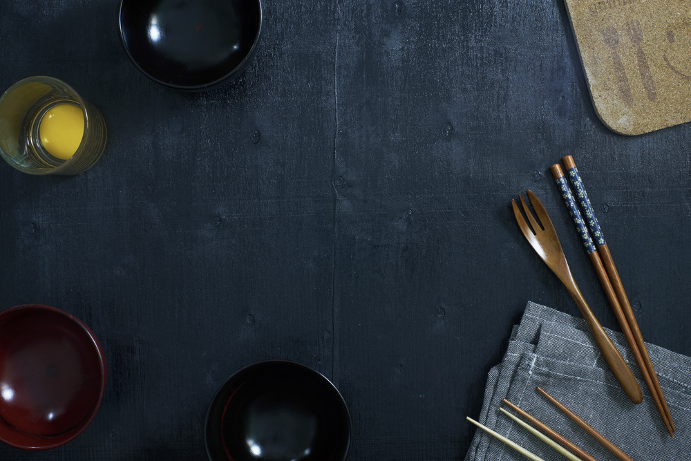 Black color wooden table top view. On the table are the Japanese wooden spoon, chopsticks, bowl,fresh raw eggs and table linen.