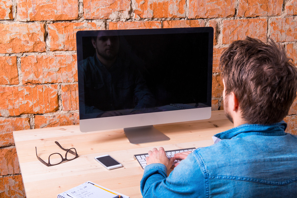 Business Person Sitting At Office Desk Working Against Brick