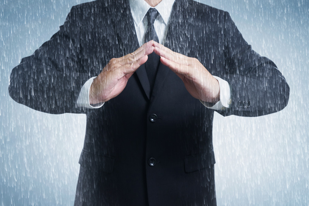Businessman in suit with two hands in position to protect in rainy weather day (focus on hand, blur out the suit). It indicates many aspects such as car insurance coverage, support, assurance, reliability.