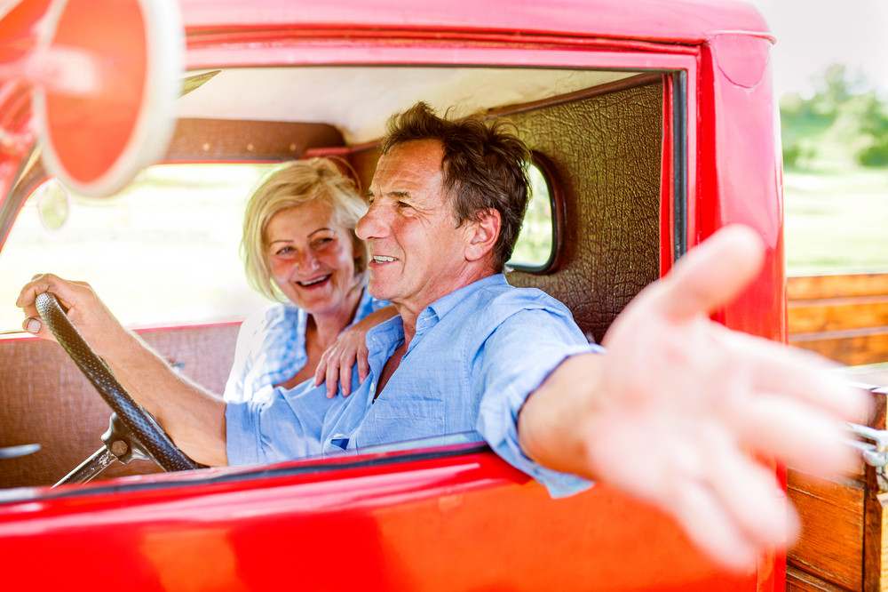 Close up of senior couple inside a red pickup truck, man holding a steering wheel, stretching out his arm