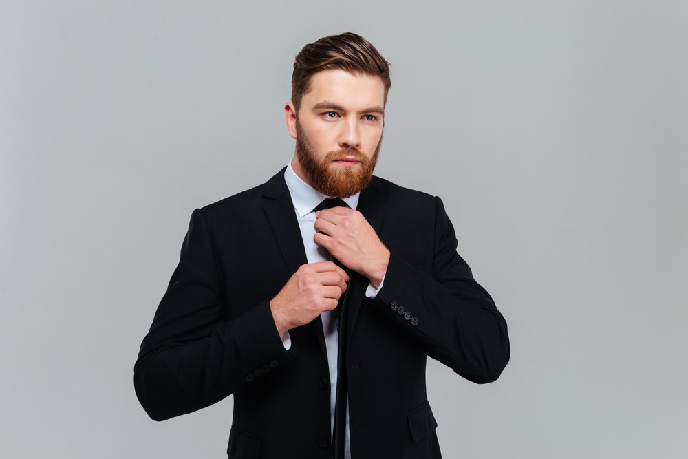 Download Cool business man in black suit tying a tie in studio ...