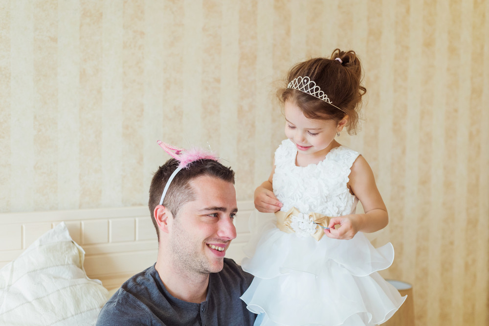 Cute little girl in princess dress putting pink crown on her father head