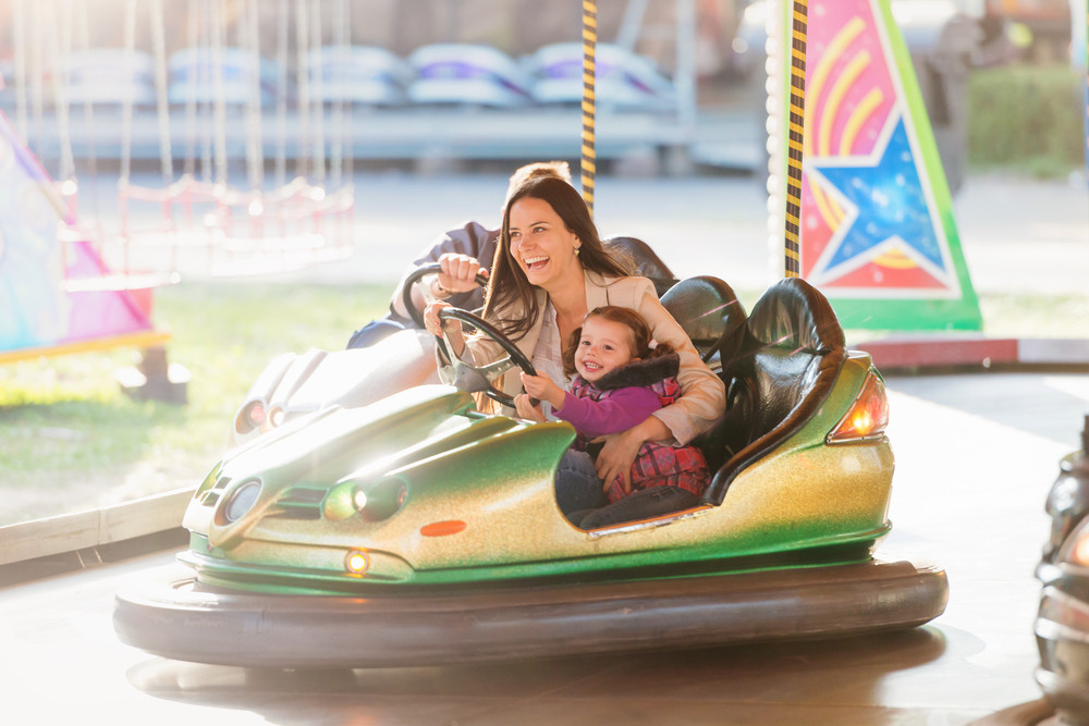 Cute little girl with her mother having fun at fun fair, driving a bumper car, amusement park