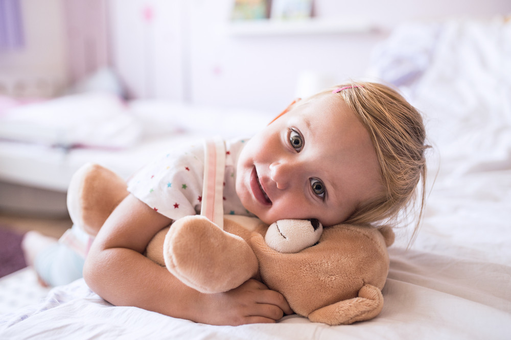 Cute little girl with her teddy bear at home lying on bed in bedroom