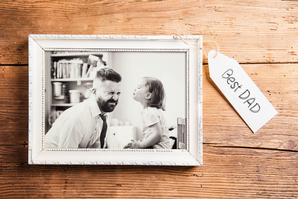 Fathers day composition. Photo of father and daughter in white picture frame. Studio shot on wooden background.