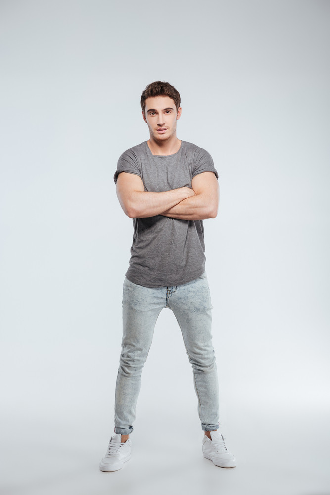 Full length portrait of a casual young man standing with arms crossed ...