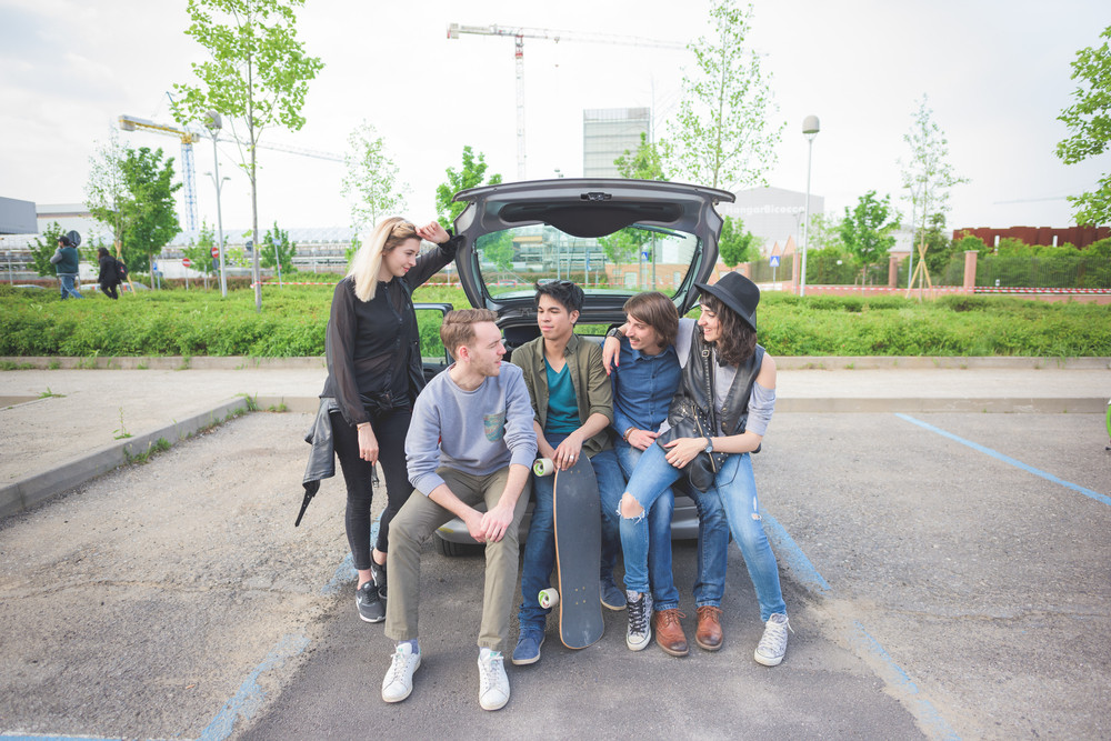 Group of young multiethnic friends sitting in a trunk of a car, talking to each other, having fun - friendship, relax concept
