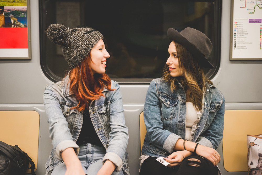 Half length of two young handsome caucasian blonde and redhead straight hair women sitting in the underground, looking one in the other eyes, chatting - friendship, transport, travelling concept
