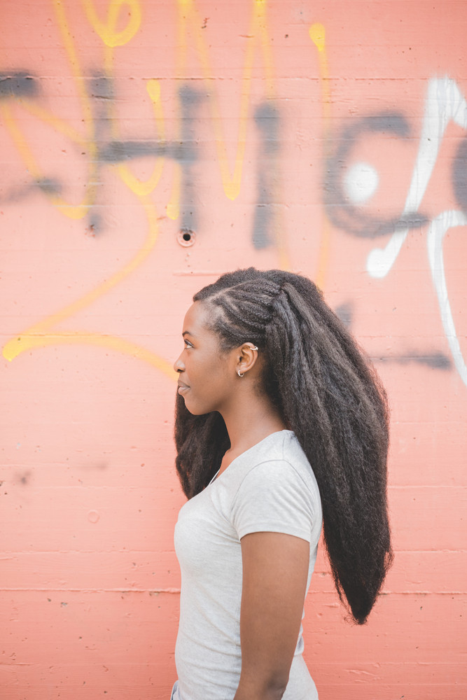Half length profile of young beautiful long brown hair black woman standing on orange wall, overlooking smiling - happiness, thoughtless concept