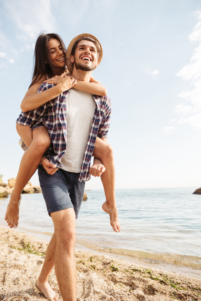 Handsome smiling young man giving piggy back ride to his girlfriend at ...