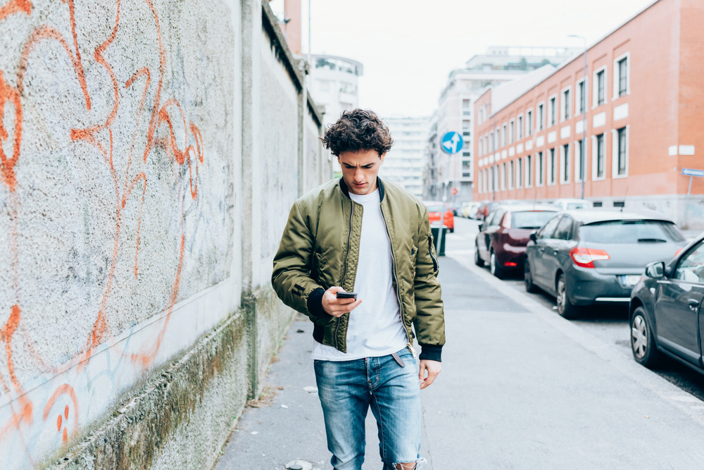 Handsome young man walking outdoor in the city using smart phone - technology, social network, city life concept
