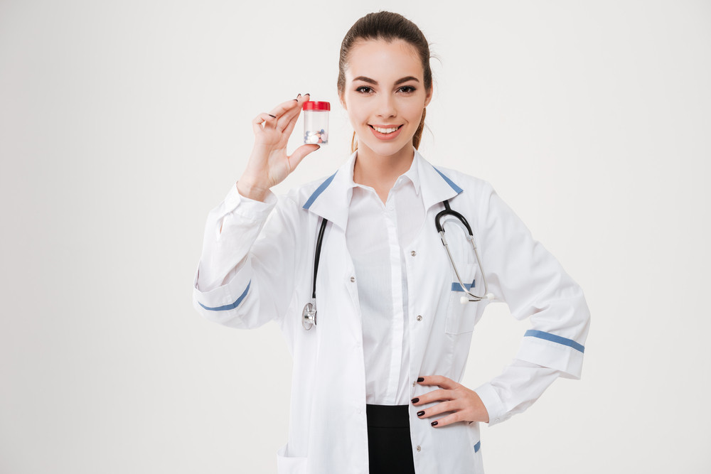 Happy charming young woman doctor holding bottle of pills over white ...