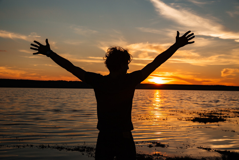 Happy Man Silhouette With Hands Up On The Sunset Background At The