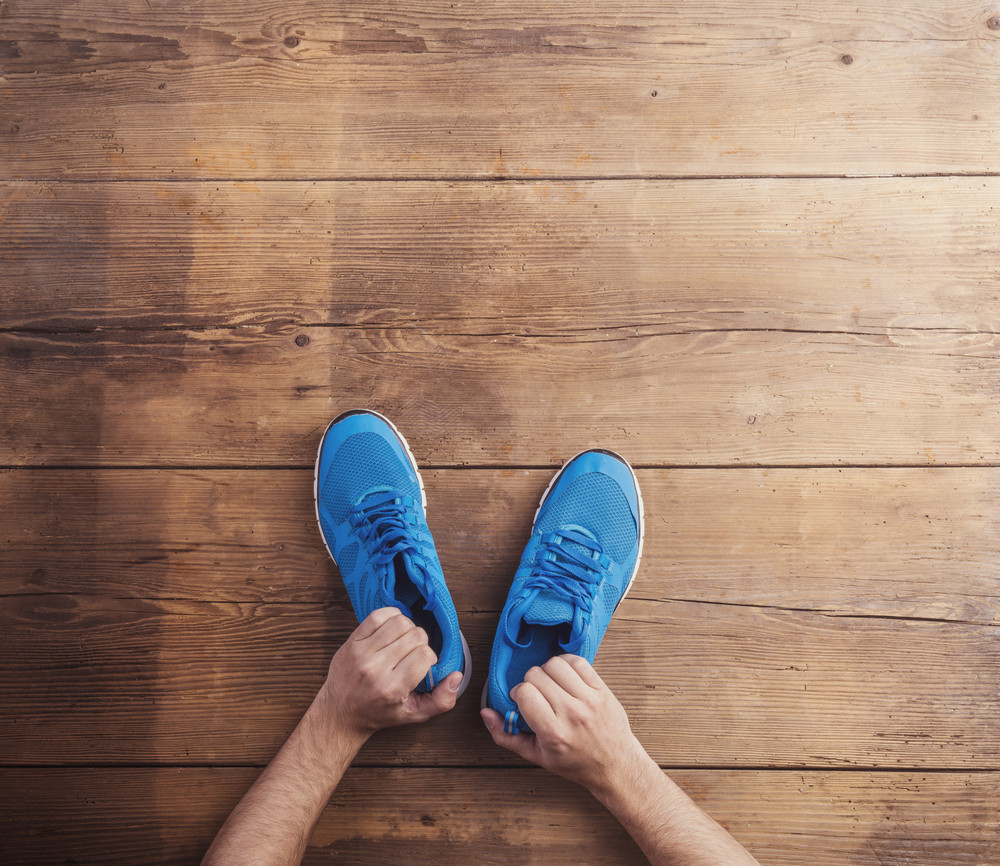 Man holding a pair of running shoes on a wooden floor background