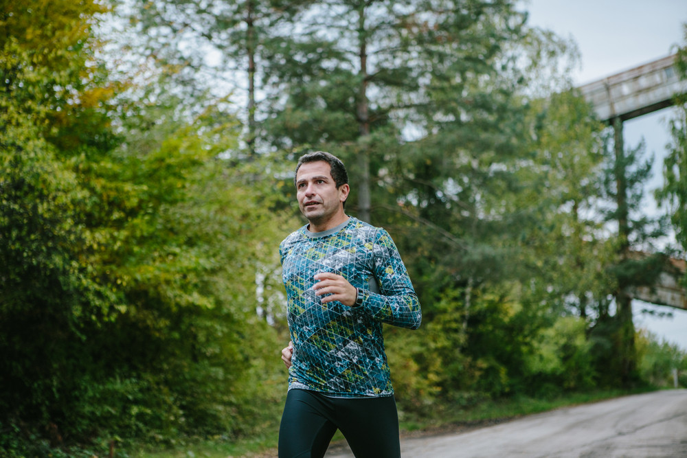 Man in sportswear running on an old road in green nature. Cloudy rainy day.
