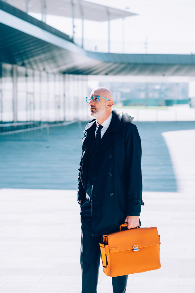 Middle-age contemporary businessman walking outdoor in the city, holding a briefcase - business, career, manager concept