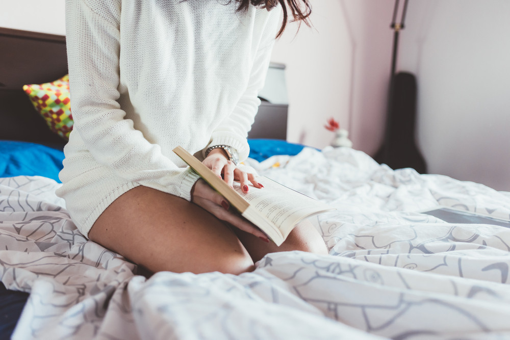 Midsection Of Young Woman Reading Book Lying On Her Bed