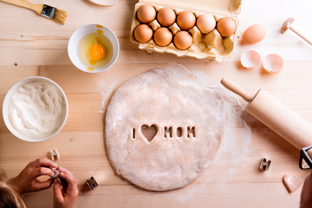 Mothers day composition. Hands of unrecognizable girl baking cookies, playing with dough. I love Mom sign made with cookie cutter. Studio shot on wooden background.