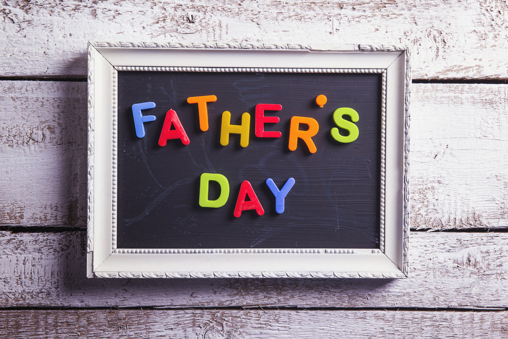 Picture frame with Fathers day sign laid on wooden floor background.