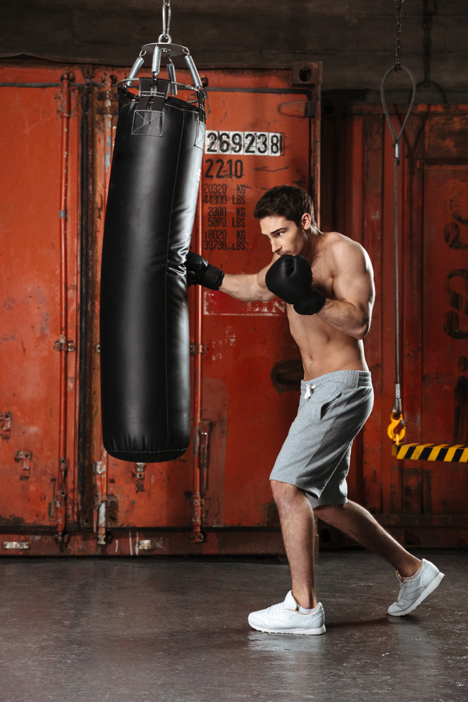 Picture of handsome young boxer training in a gym with punchbag ...