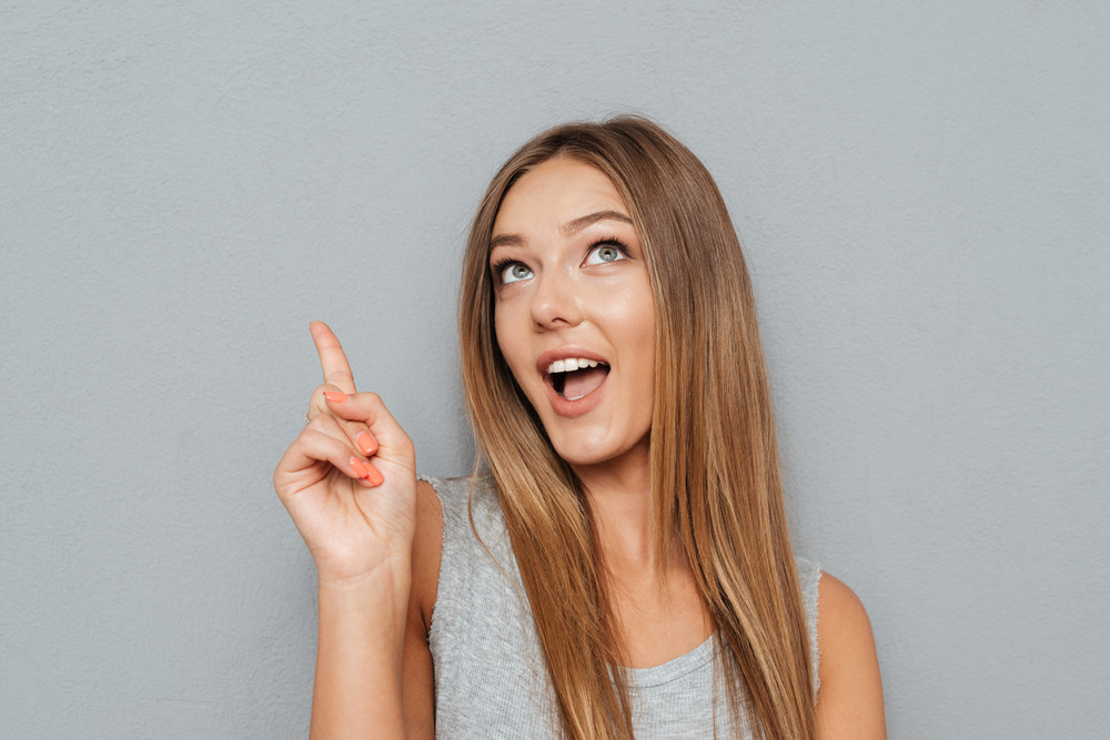 Portrait Of A Smiling Girl Pointing Finger Up At Copyspace Isolated On 