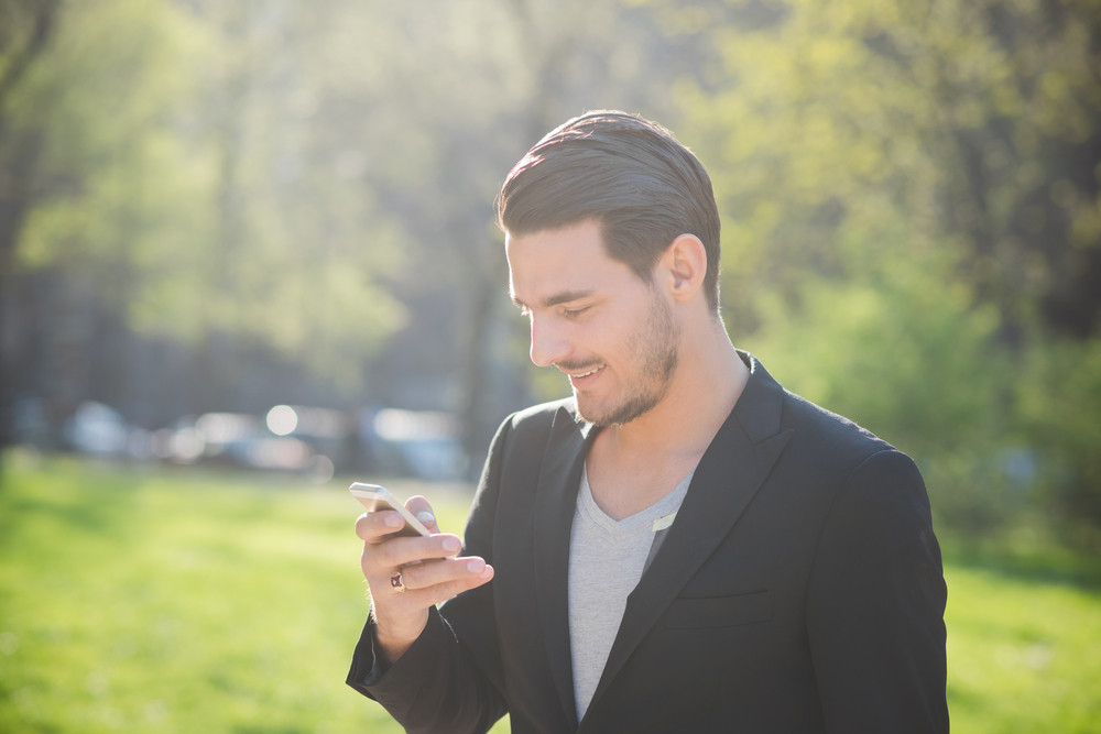 Portrait of a young handsome caucasian man using a smart phone connected online, looking down and tapping the screen- technology, social network concept