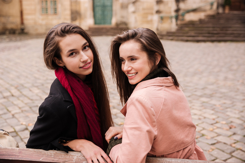 Portrait of two happy beautiful young women sitting together in old ...