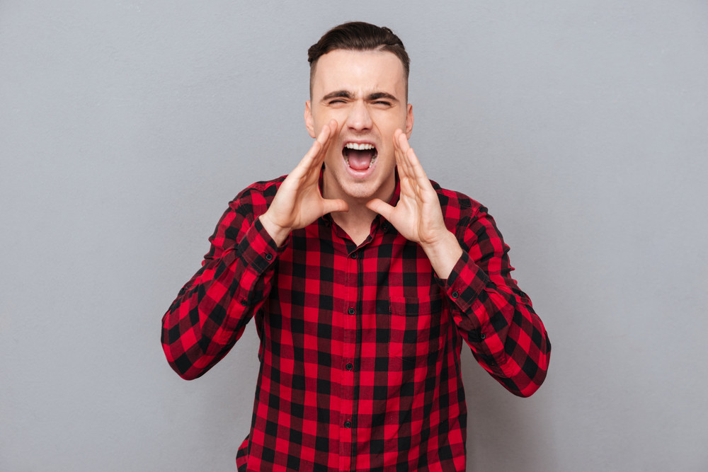 Screaming young man in shirtholding hands near the face and looking at camera. isolated gray background