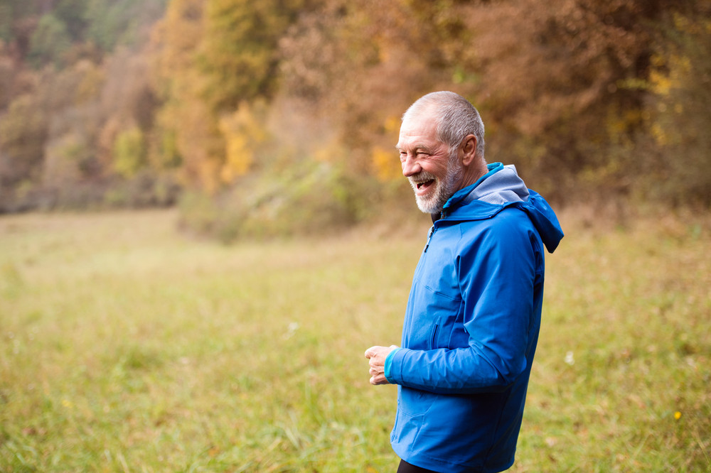 Senior runner in blue jacket resting outside in sunny autumn nature, laughing.