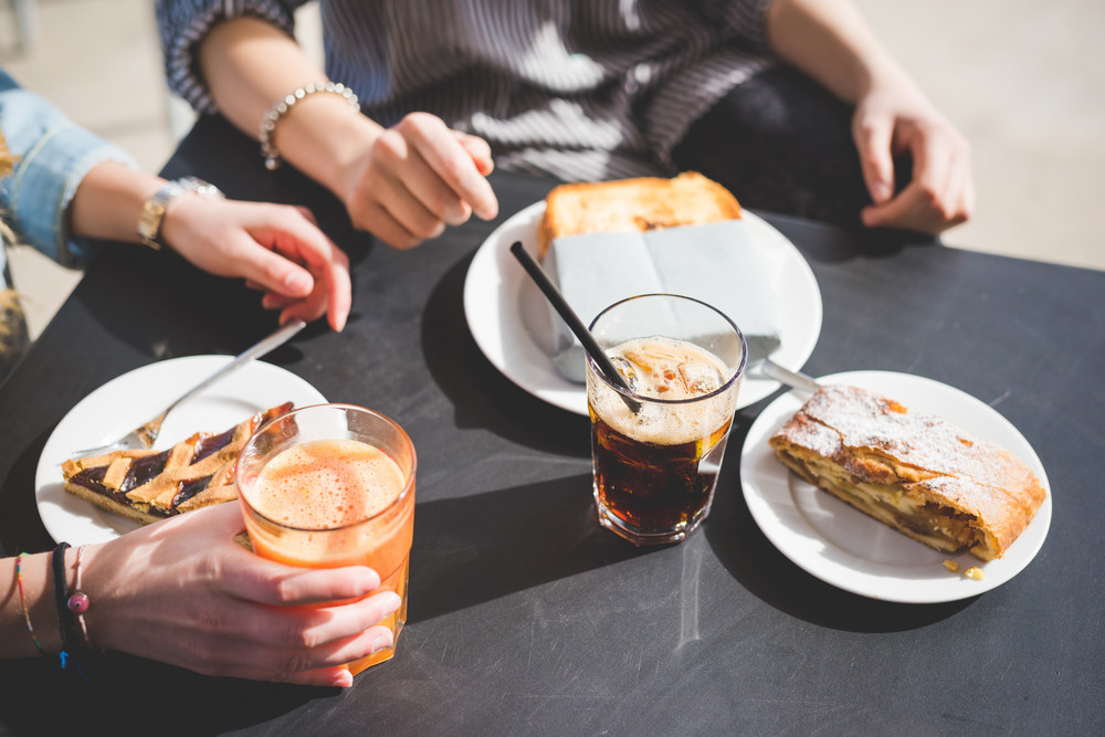 Two women friends having an happy hour in a bar - focus on the table with cake, toast and juice - aperitif, snack, relaxing concept