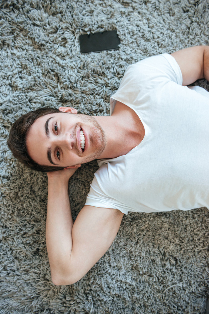 Vertical Image Of Happy Man Lying On The Floor And Looking At
