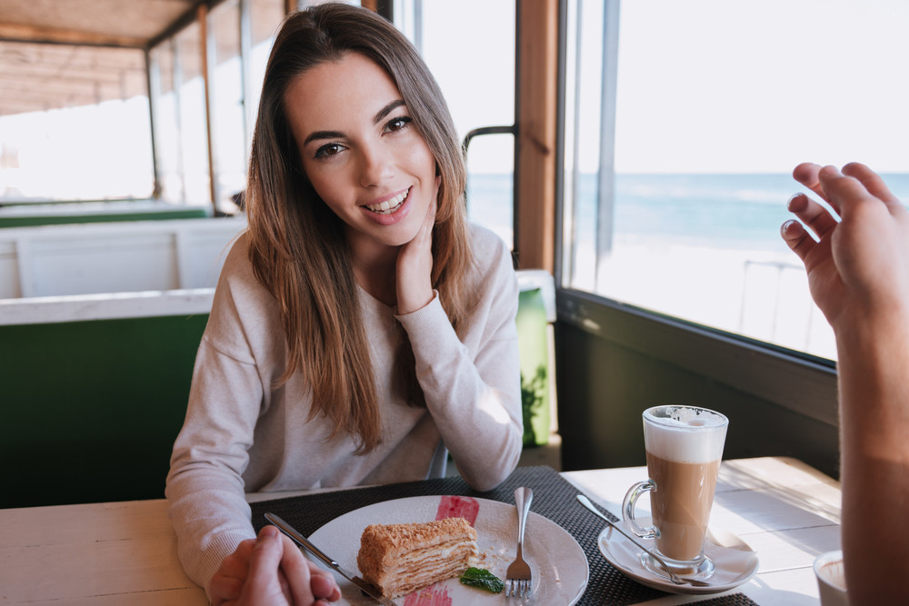 Woman sitting by the table with food on date in cafe near the sea ...