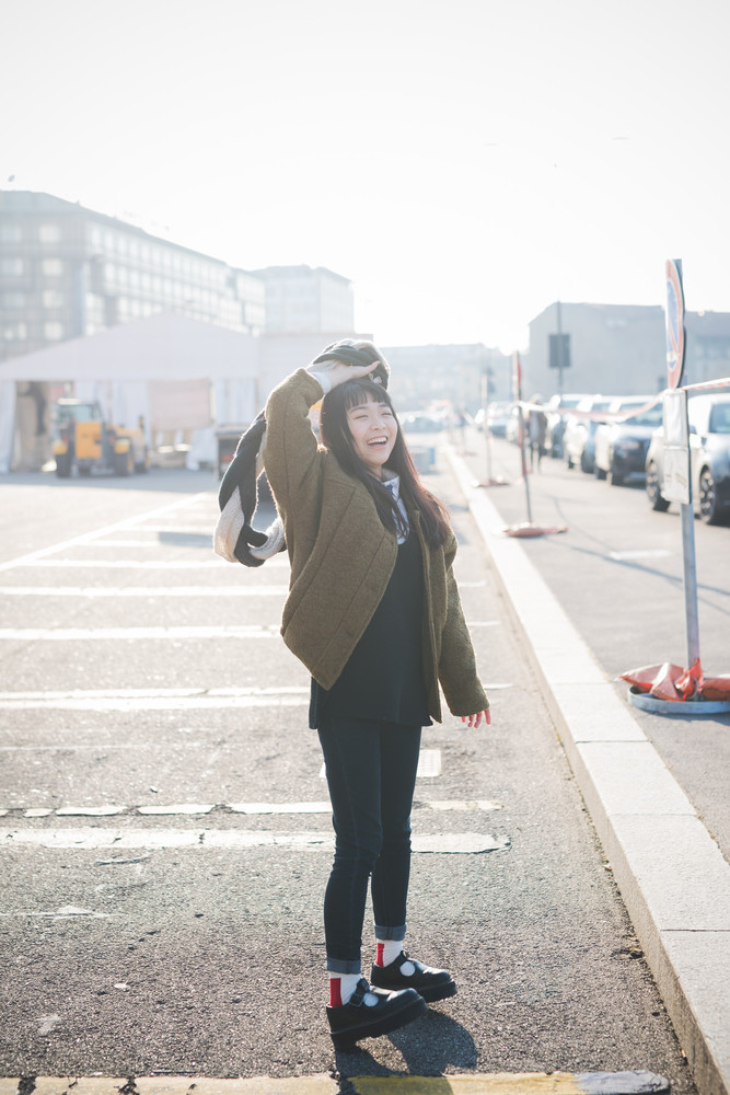young beautiful asian hipster woman in the city - living town during sunset in backlit - smiling happy having fun with scarf