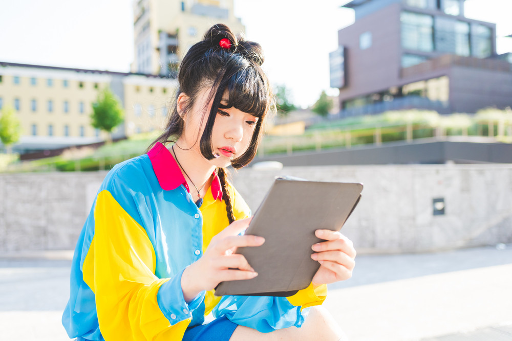 young beautiful asian millennial woman nonconformist outdoor in the city holding a tablet looking the screen - technology, social network, communication concept