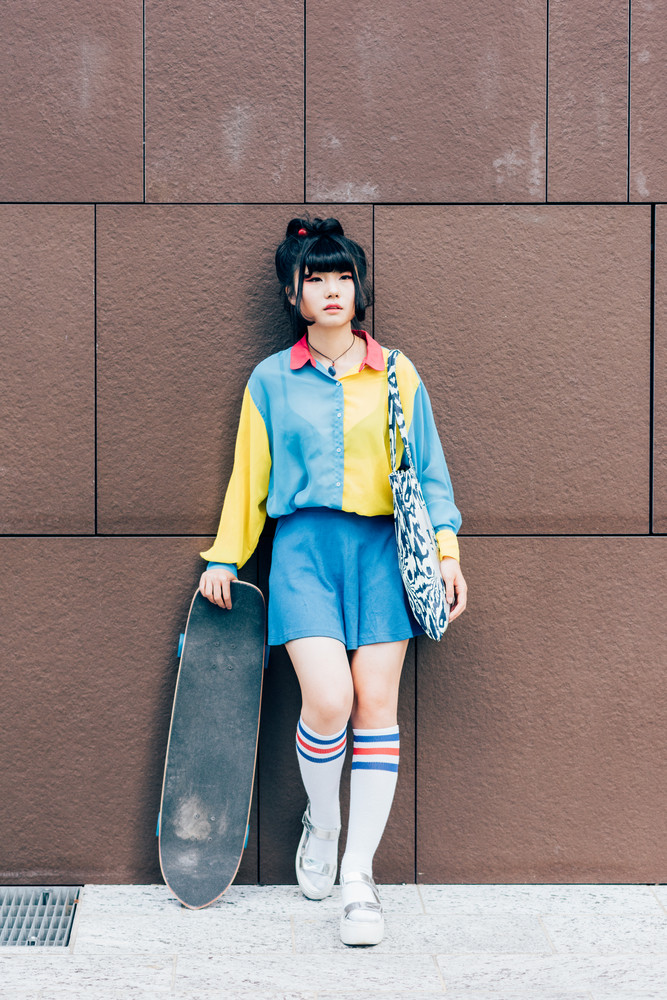 young beautiful asian millennial woman nonconformist skater posing outdoor in the city holding skateboard - eccentric, sportive concept