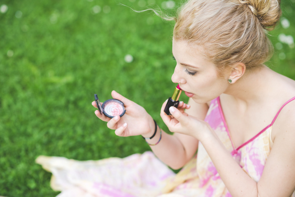 Young beautiful caucasian pale blonde hair woman outdoor putting make up on - vanity, beauty, skin care concept